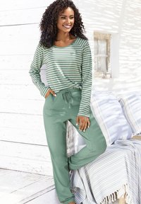 Garās piedurknes zaļi un balti svītrainā blūze, saskaņota ar vienkrāsainām zaļām biksēm. Materiāls izskatās mīksts, redzami kabatas un brīvs griezums.