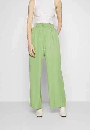 Hellgrüne Weitbein-Hosen mit hoher Taille, Falten und Knopfverschluss. Kombiniert mit einem weißen, gerippten Crop-Top und neutralen Schuhen.