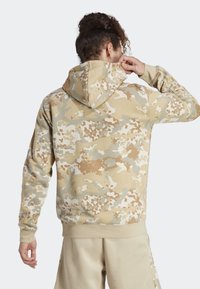 Sudadera con capucha de camuflaje beige con cordón, que presenta un tejido texturizado y un corte relajado. Los puños y el dobladillo acanalados completan el diseño.