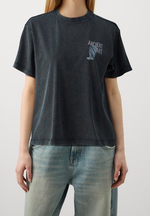 Osoba ubrana w wyblakły czarny T-shirt z napisem "ANCIENT ART" i ilustracją popiersia na piersi, w połączeniu z jasnoniebieskimi dżinsami.