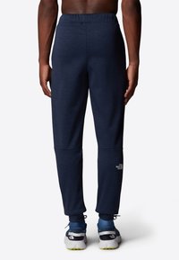 Marinblå sweatpants med elastisk midja, smalnande design och kontrasterande logotypdetalj på underbenet, i kombination med träningsskor.