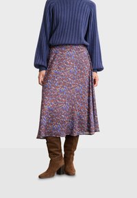 Utsvängd, knälång kjol i ett mönstrat tyg med blått, rött och brunt. Matchad med knähöga bruna mocka stövlar och en ribbade tröja.