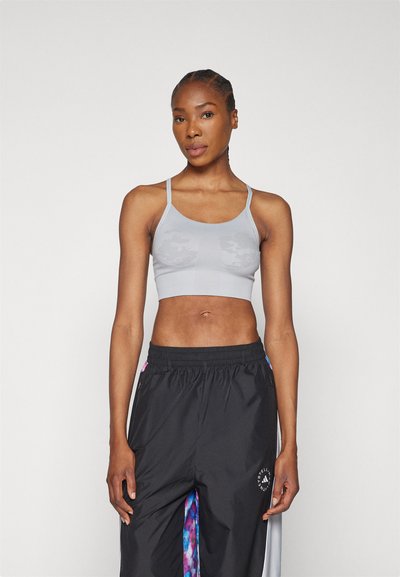 Sivé skrátené športové podprsenky s tenkými ramienkami, textúrovaným povrchom a jemným vzorom. V kombinácii s �čiernymi voľnými športovými nohavicami s farebnými akcentmi.