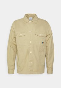 Chaqueta de algodón beige con cierre de botones, dos bolsillos en el pecho y dos bolsillos laterales. Presenta un logo bordado multicolor en el pecho izquierdo.