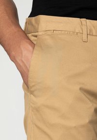 Khaki chinos o gładkiej fakturze, z przednią kieszenią i płaskim pasem. Materiał jest trwały i lekki.