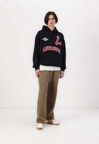 Black hoodie with red graphics, including "LOWLIGHTS" and a logo. Paired with loose beige pants and white sneakers with red stripes.