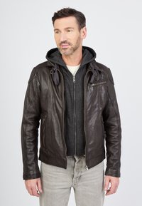 Ruskea nahkatakki vetoketjulla, jossa on harmaa huppari alla, näkyvät ompeleet ja sivutaskut, yhdistettynä vaaleanharmaisiin farkkuihin.