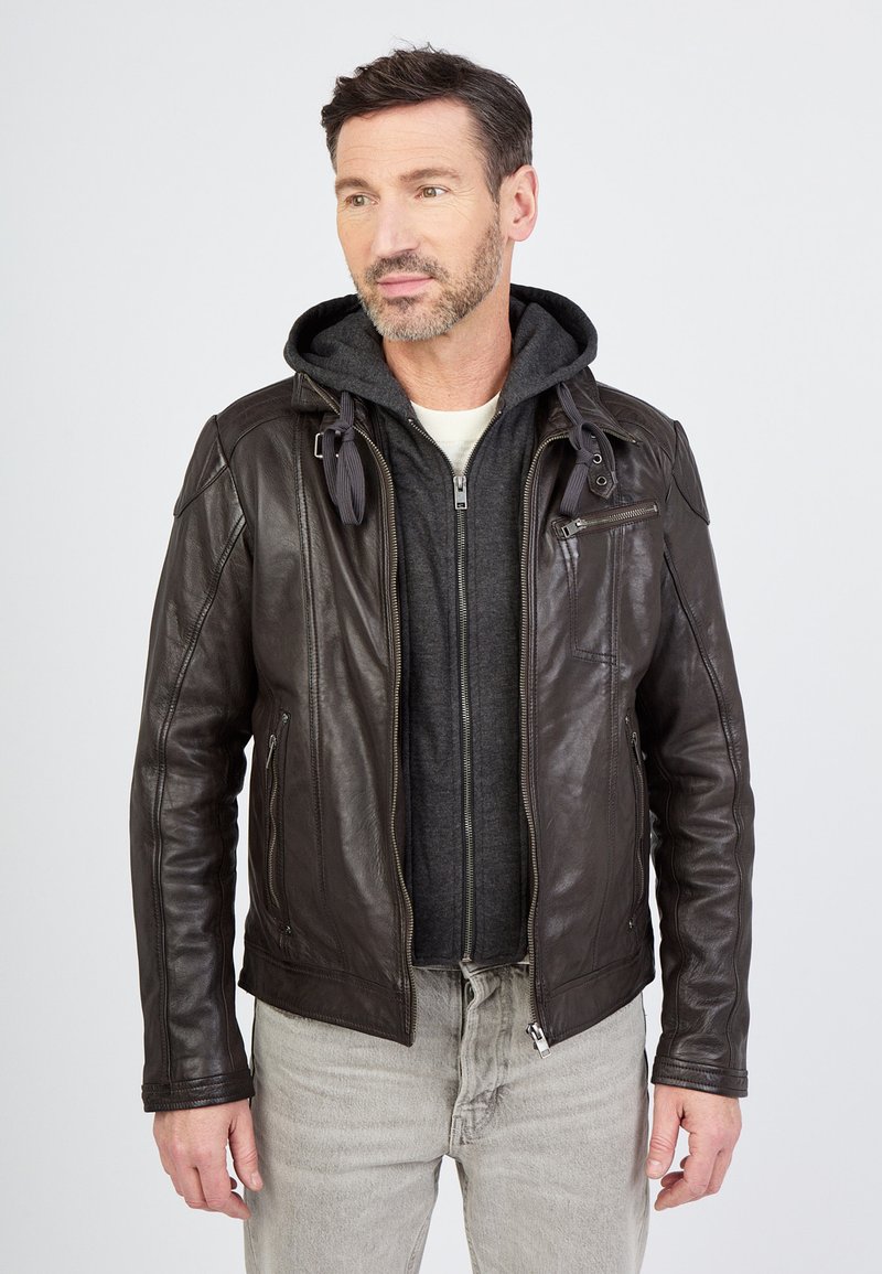 Ruskea nahkatakki vetoketjulla, jossa on harmaa huppari alla, näkyvät ompeleet ja sivutaskut, yhdistettynä vaaleanharmaisiin farkkuihin.