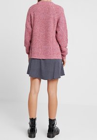 Maglione rosa lavorato a maglia con una finitura testurizzata, abbinato a una gonna nera a pois. Il modello indossa stivaletti neri alla caviglia.