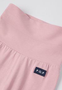 Vaalea vaaleanpunainen kangas, jossa on leveä vyötärönauha ja pieni tummansininen etiketti, jossa lukee "P.O.P", ommeltuna sauman lähelle.