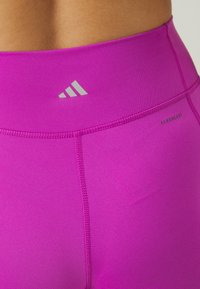 Leggings sportivi di un brillante colore rosa, realizzati in materiale elasticizzato, dotati di una vita alta con un logo grigio e cuciture senza soluzione di continuità per garantire comfort.