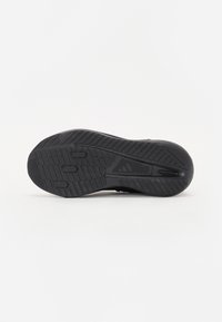 Semelle de chaussure de sport noire en caoutchouc texturé, dotée d'un motif de rainures et d'indentations circulaires pour une adhérence optimale. Bords lisses et bout arrondi.