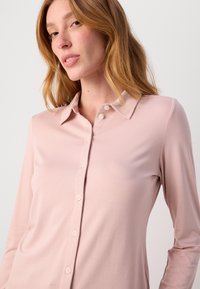 Lys rosa langermet skjorte med krage, preget av en jevn tekstur og fem matchende knapper nedover fronten.