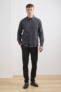 Chemise à boutons en tissu gris foncé, associée à un pantalon noir slim. La chemise possède un col et des boutons en bois, portée avec des chaussures noires.