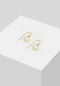 Goldfarbene Ohrringe mit einem gebogenen Haken-Design und runden weißen Steinglasuren. Minimalistischer Stil mit glatten Texturen und einer polierten Oberfläche.