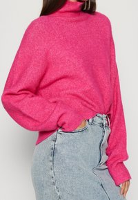 Růžový rolák s měkkou texturou, volnější střih a dlouhé rukávy, doplněný světle modrou denimovou sukni.