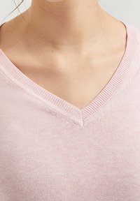 Close-up of a person wearing a light pink V-neck knit sweater, focused on the neckline and upper chest area.