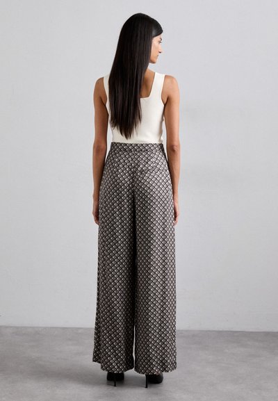 Breda byxor med geometriskt mönster i svart och beige, med hög midja och slät tygtextur. Stylar med en figurnära ärmlös topp.