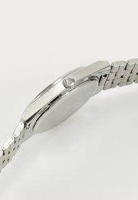 Orologio in acciaio inox argentato con cassa rotonda, superficie texturizzata e design della bracciale a maglie. Presenta una corona prominente sul lato.