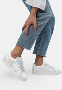 Baskets blanches avec un motif d'étoile argentée et des accents cloutés, présentant un dessus en cuir lisse, un design à lacets et une semelle en caoutchouc contrastante.