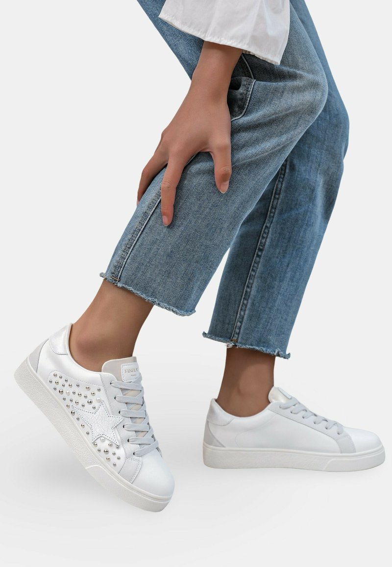 Baskets blanches avec un motif d'étoile argentée et des accents cloutés, présentant un dessus en cuir lisse, un design à lacets et une semelle en caoutchouc contrastante.