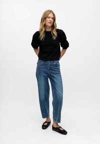 Maglione nero con maniche a sbuffo, jeans blu a gamba dritta e scarpe nere. Tessuto morbido con una vestibilità casual e dettagli minimi.