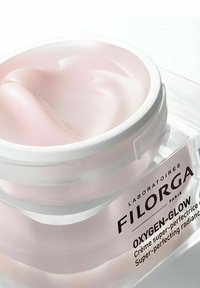 Filorga Oxygen-Glow cream in a clear, round jar with a white lid, displaying a smooth, pale pink gel texture inside.