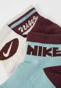 Meias de crew com punhos canelados, feitas de uma mistura de tecidos brancos, bordeaux e azul claro, com logótipos da Nike em cores contrastantes.