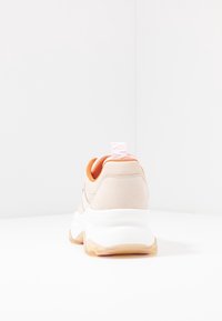 Sneaker beige con una texture morbida, caratterizzata da una suola intermedia bianca, allacciatura arancione e un tassello posteriore rosa. Design solido con branding minimale.