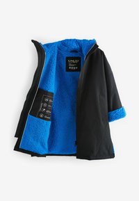 Svart ytterjacka med blå fleecefoder, dragkedjestängning och etikett för skötsel inuti. Detaljer inkluderar ett texturerat fleece-material och sömmar på ärmarna.