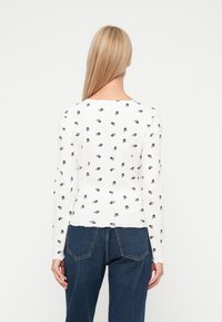 Λευκό ριγωτό πουλόβερ με διάσπαρτο μικρό μπλε λουλουδάκι. Μακριά μανίκια και στρογγυλή λαιμόκοψη. Φορεμένο με τζιν παντελόνι ψηλής μέσης.