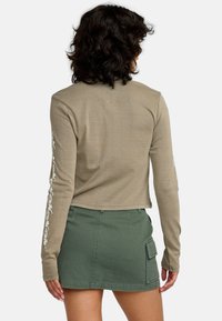Khaki langekleurige top met bloemborduursel langs de mouwen, gecombineerd met een groene cargobroek met voorzakken en een strakke taille.