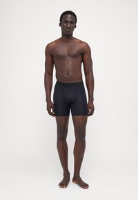 Fekete boxer alsónadrág elasztikus derékrésszel, sima textúrával és testhezálló kialakítással, férfi modellen bemutatva, semleges háttér előtt.