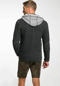 Cardigan tricoté gris foncé avec une capuche gris clair. Comprend des patchs aux coudes. Tissu texturé, poignets et ourlet côtelés, design minimaliste.