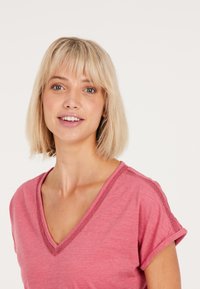 Top a maniche corte con scollatura a V in morbido tessuto rosa, con dettagli testurizzati lungo il collo. Presenta una vestibilità comoda e maniche arrotolate.