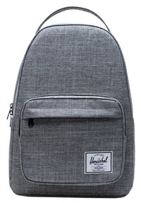 Mochila de tela gris con una textura suave, parte superior redondeada, bolsillo frontal con cremallera y un parche con logo. Diseño simple con un asa única en la parte superior.