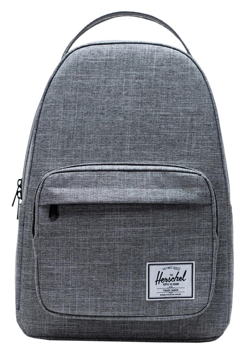Mochila de tela gris con una textura suave, parte superior redondeada, bolsillo frontal con cremallera y un parche con logo. Diseño simple con un asa única en la parte superior.