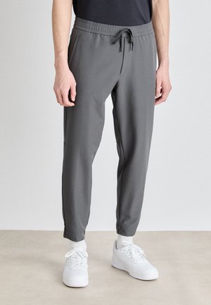 Gray athletic jogger pants with an elastic waistband and drawstring, featuring side pockets and tapered cuffs, paired with white sneakers.