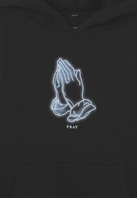 Felpa nera con cappuccio caratterizzata da una grafica di mani in preghiera contornata di bianco e la parola "PRAY" sottostante. Tessuto morbido con tasca a marsupio.