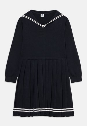 Robe plissée bleu marine à manches longues avec col marin et double rayures blanches sur le col et l'ourlet sur fond uni.