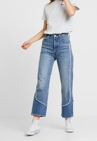 Denimjeans med høj talje og lyseblå vask, brede ben, frynset kant og kontrasterende sidesømme. Kombineret med en grå t-shirt.