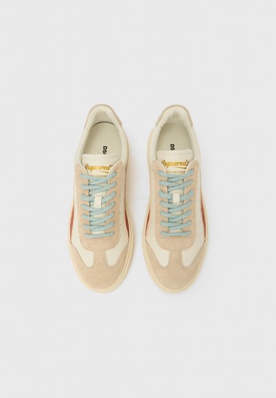 Beige suède en crème kleurige leren sneakers met lichtblauwe veters, met een rode accentstreep en een gouden logo op de tong. Zacht en gestructureerd bovenwerk.