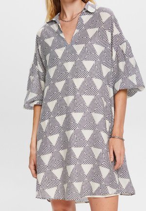 Mujer con un vestido suelto con un patrón geométrico de triángulos en blanco y negro y mangas abullonadas de longitud media.