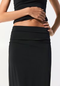 Un débardeur noir ajusté et une longue jupe avec une taille froncée, fabriqués dans un tissu lisse et extensible, présentant une silhouette épurée.