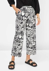 Zwart-witte bloemenprint wijde broek met een gladde stof en zijzakken, gecombineerd met zwarte slide-sandalen met gespen.