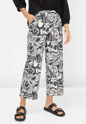 Zwart-witte bloemenprint wijde broek met een gladde stof en zijzakken, gecombineerd met zwarte slide-sandalen met gespen.