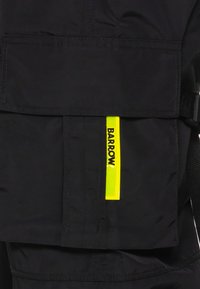 Zwarte stoffen tas met een opvallend geel "BARROW" label. Beschikt over een grote zak en getextureerde schouderbanden voor het dragen. Minimalistisch ontwerp.