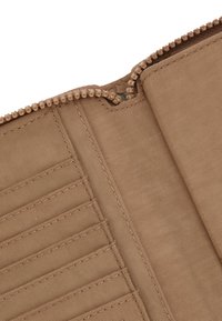 Portafoglio beige con zip, dotato di un esterno in tessuto, con scomparti per carte e una superficie interna liscia. Il dettaglio della zip è visibile lungo il bordo.
