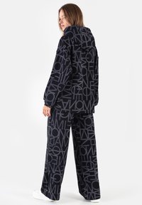 Czarny i szary zestaw z dużymi wzorami logo, składający się z kurtki z kapturem i szerokich spodni. Gładka faktura.