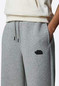 Harmaat collegehousut, joissa on joustava vyötärönyöri, sivutaskut ja musta kohokuvioitu logo reidessä. Pehmeä kankaan tekstuuri.